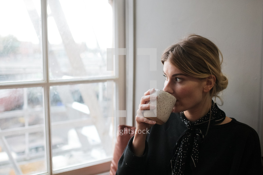 a woman drinking coffee by a window 