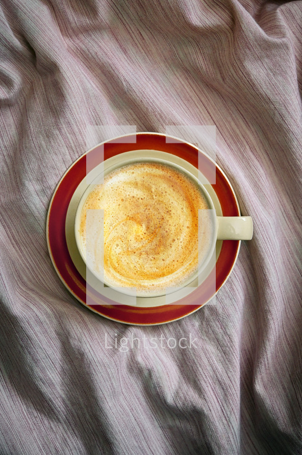 Flat lay of a cup of cappuccino coffee in bed on crumpled sheets