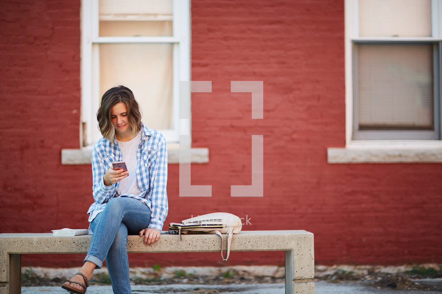 a woman sitting on a stone bench looking at her cellphone 