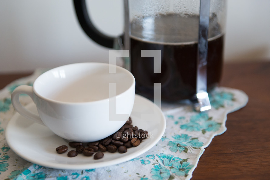 Coffee beans on a saucer with an empty coffee cup next to a carafe of coffee,