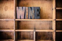 Wooden letters spelling "wine" on a wooden bookshelf.