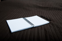 blank pages of an opened notebook on a bed 