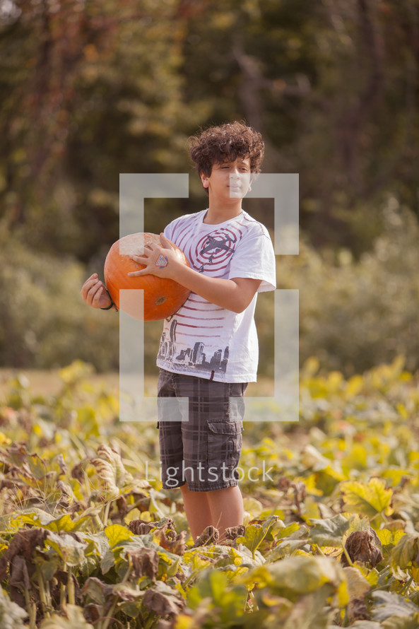 boy child picking out a pumpkin in a pumpkin patch 