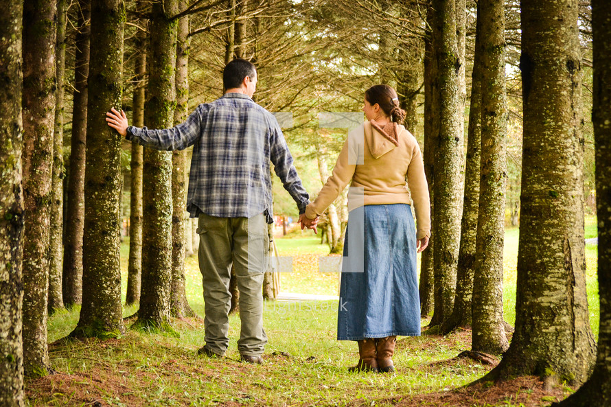a couple walking holding hands through a forest 