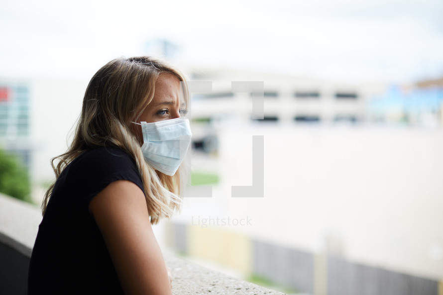 a young woman wearing a face mask looking over a railing 