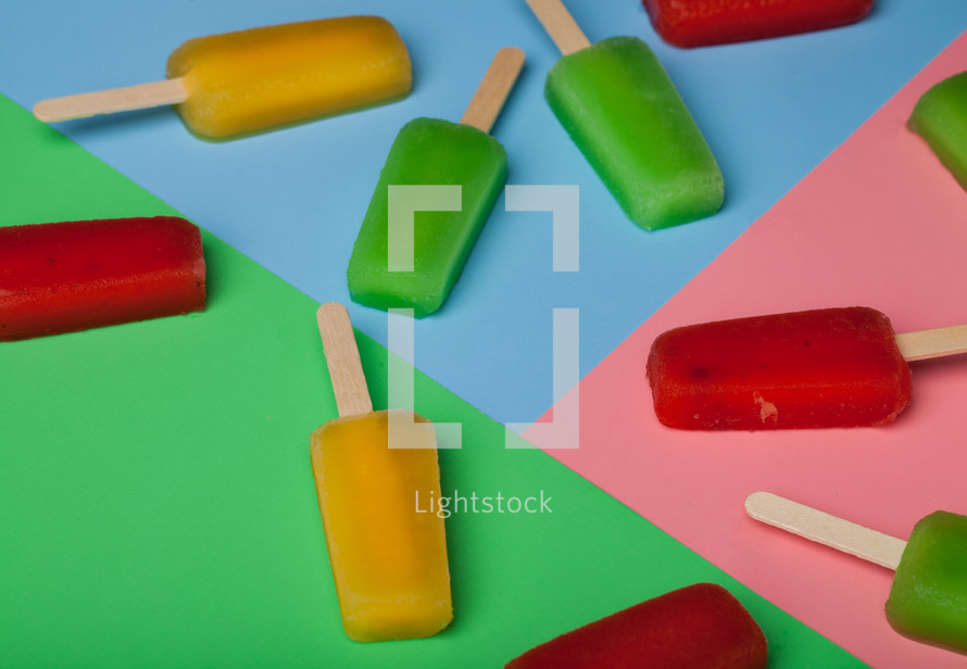 Brightly colored popsicles arranged on brightly colored paper.