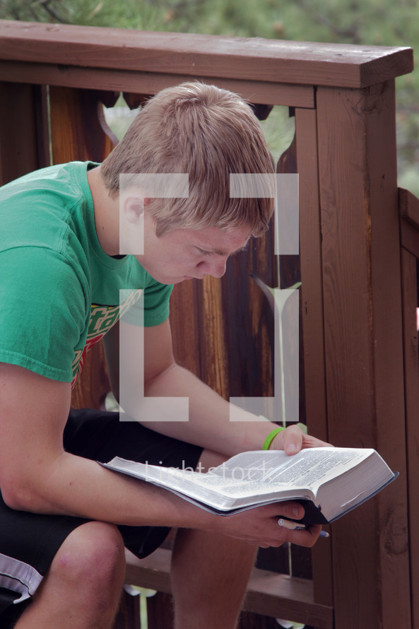 young man reading a Bible on a porch 