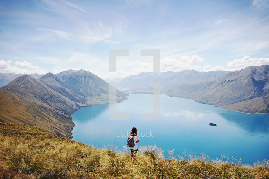 a woman looking down at a lake surrounded by mountains 