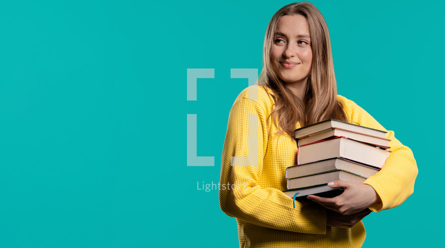 Smiling student woman with stack books from library, blue background. Copy space. Happy girl smiles, she is happy to graduate. High quality