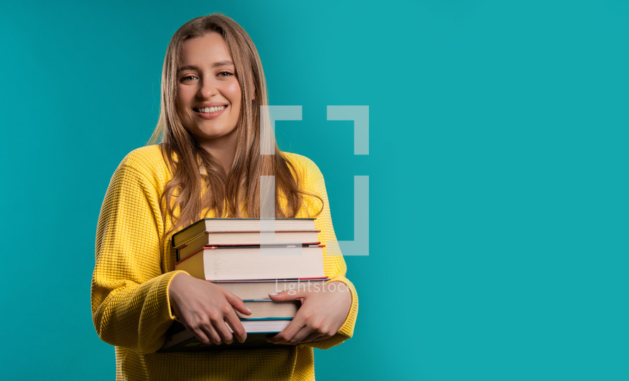 Smiling student woman with stack books from library, blue background. Copy space. Happy girl smiles, she is happy to graduate. High quality