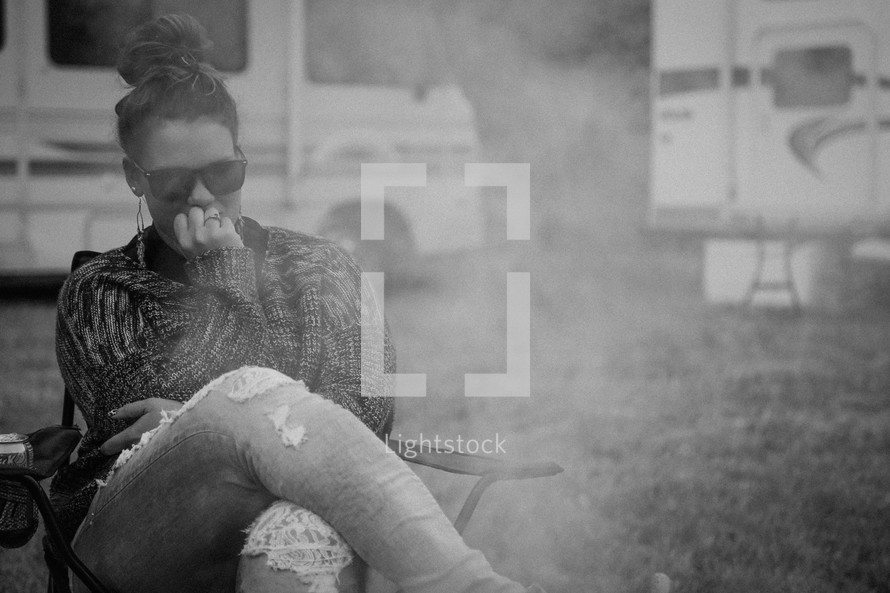 a woman sitting in a chair around smoke from a campfire 
