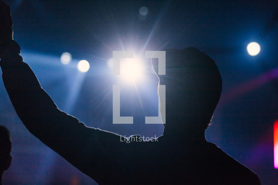 silhouette of a man with hands raised at a concert 