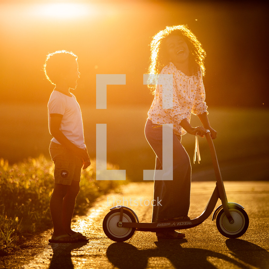 kids in warm sunlight with a scooter 