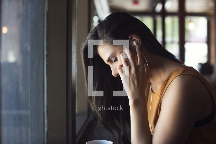 a young woman listening to earbuds in front of a window 