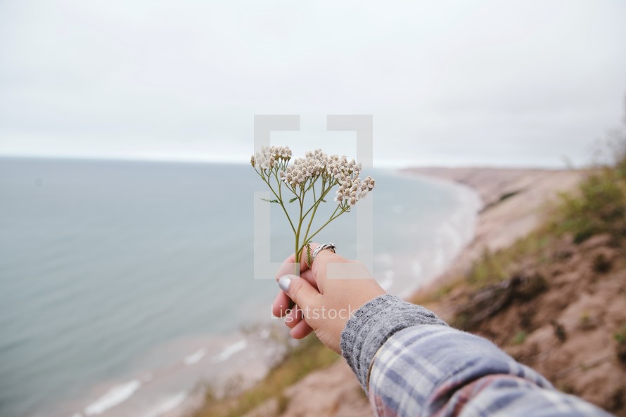 woman holding out picked flowers above a shore 
