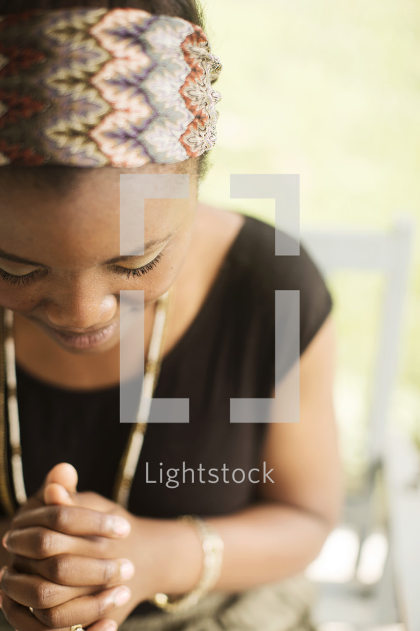 African-American teen sitting outside on a porch swing happily praying.
