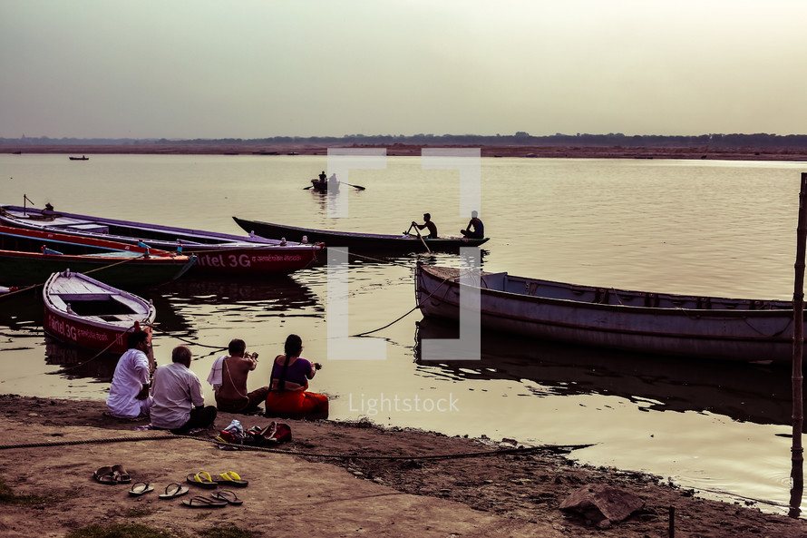 fishing boats and people sitting along a shore 