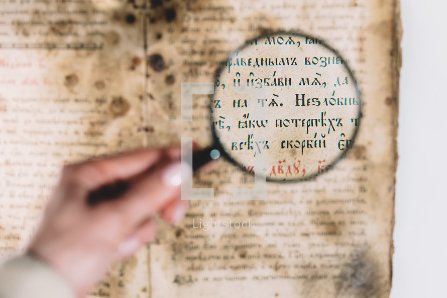 Woman researcher explores antique book with magnifier. Scientific translation of literature. Investigating manuscript with ancient writings