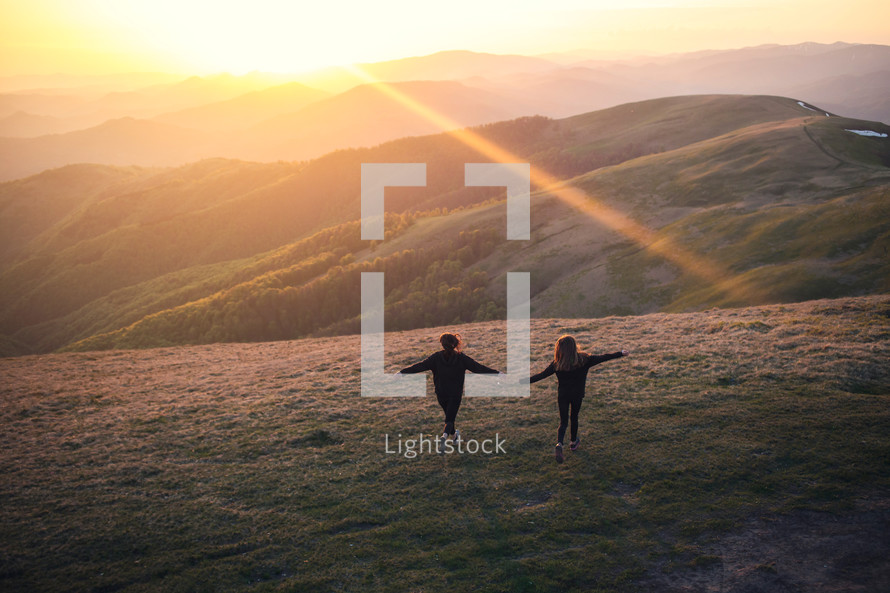 girls standing on a mountaintop at sunrise with outstretched arms 