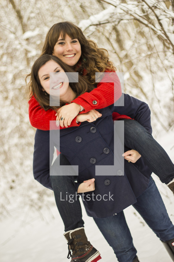 One girl holding another girl on her back, out in the snow