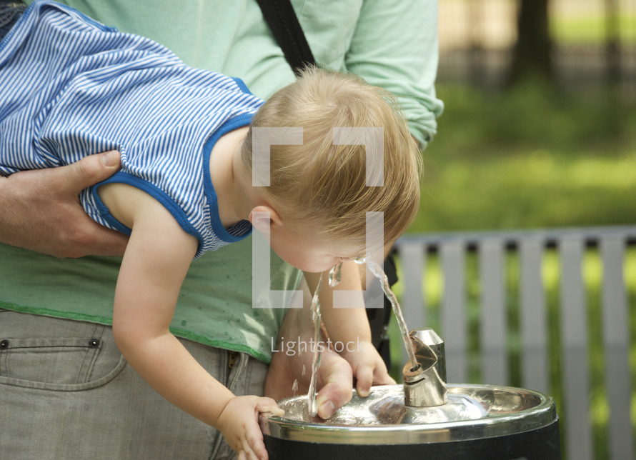A man holding a young child up to a water fountain.