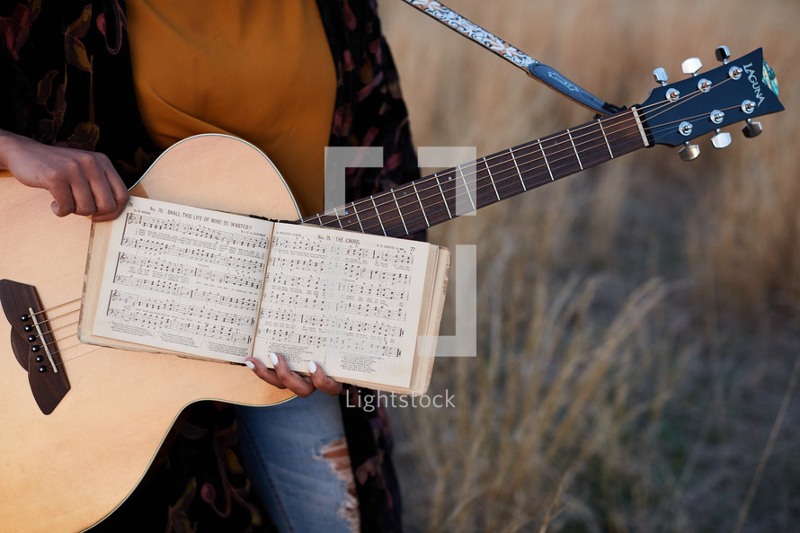 a woman standing in a field with a guitar and sheet music 