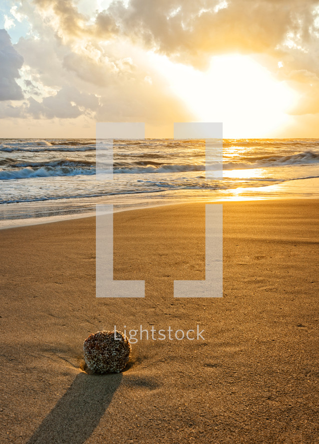 a rock on a beach in sand at sunset 