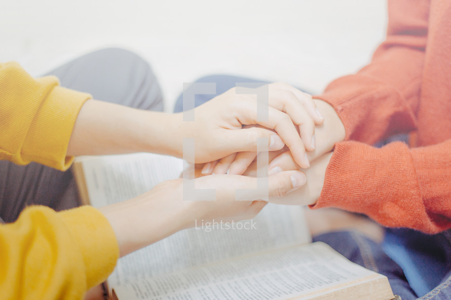 a couple holding hands and praying over a Bible 