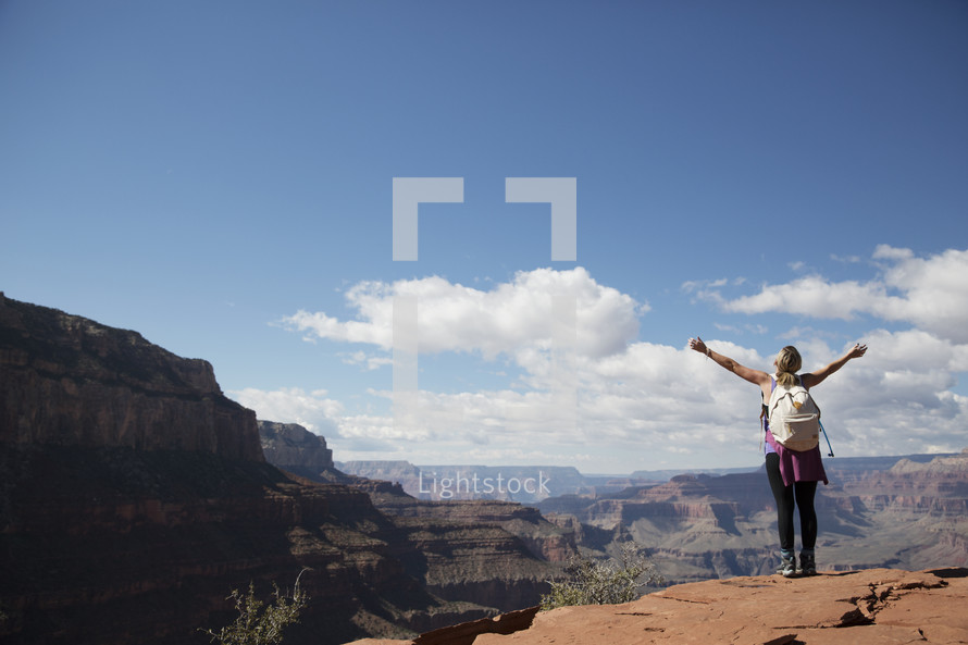 woman standing at the edge of a canyon cliff with raised arms 