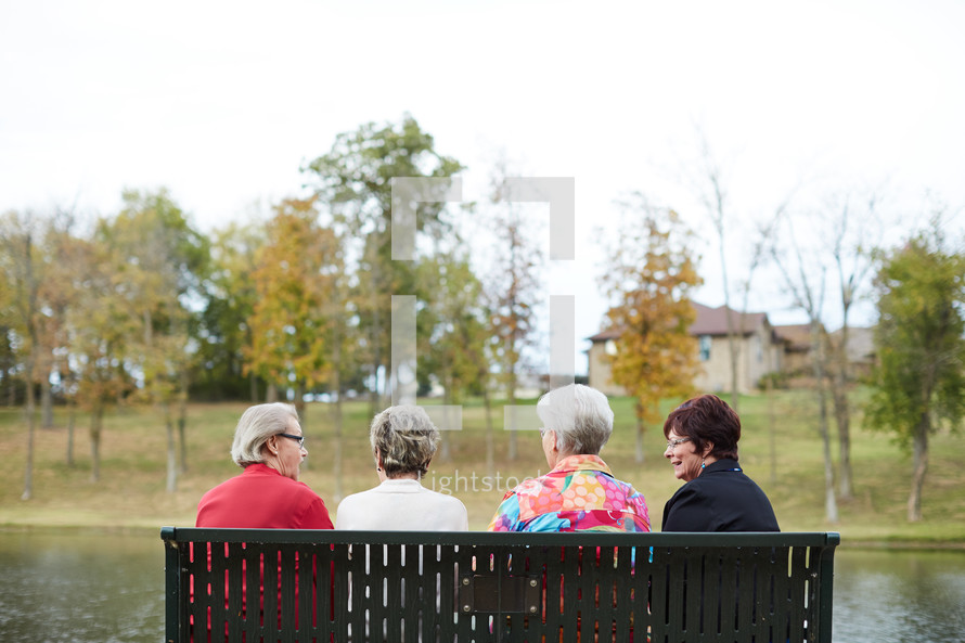 elderly women sitting on a park bench talking 
