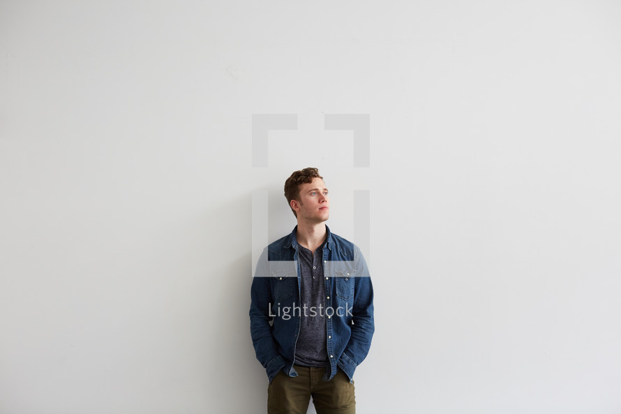 a man looking up and thinking against a white wall.