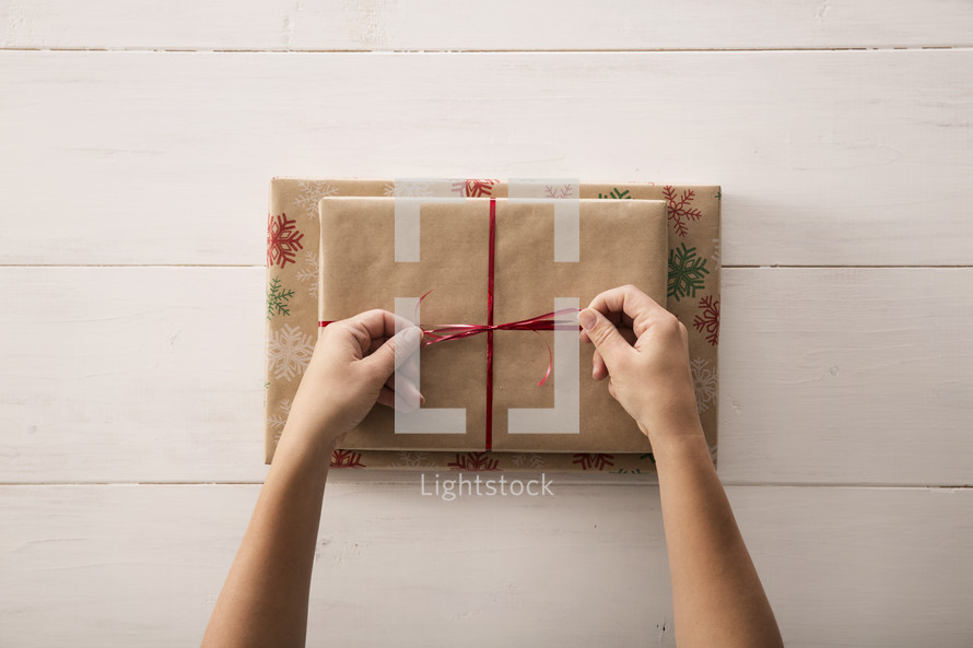 Tying a red ribbon on a wrapped gift.