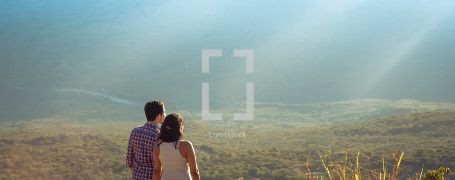 man and woman looking at bright sunlight over a valley  