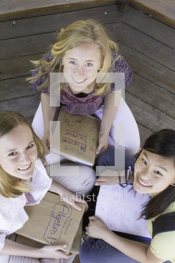 Teen girls sitting on wood floor studying with text books.
