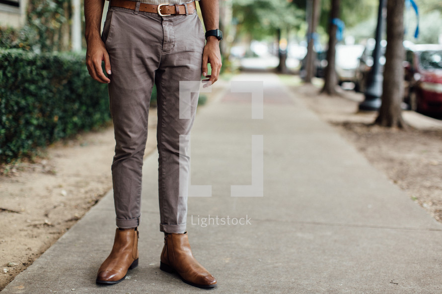 legs of a man standing on a sidewalk downtown 