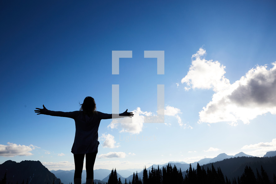 a woman standing with outstretched arms taking in a mountain view 