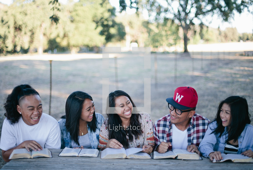 friends reading Bibles together outdoors at a picnic table 