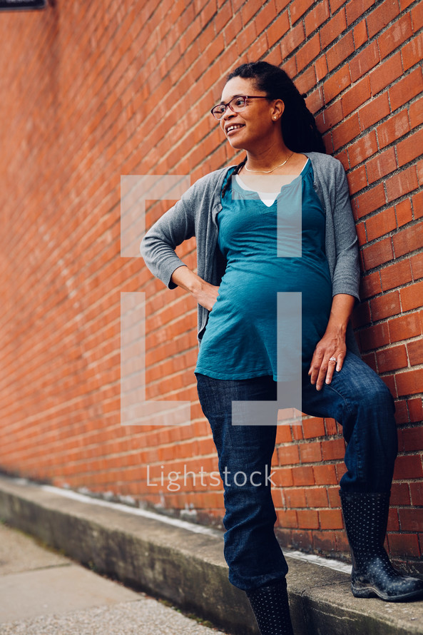 Pregnant African-American Woman standing against a brick exterior wall