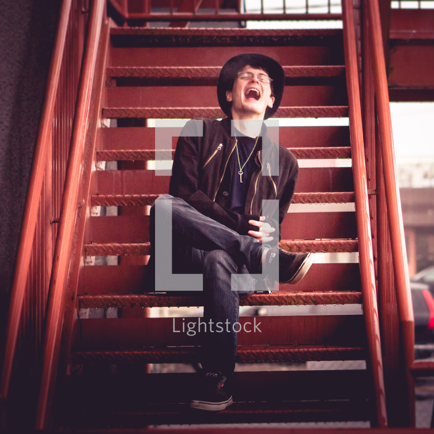 A laughing young man sitting on a metal staircase.
