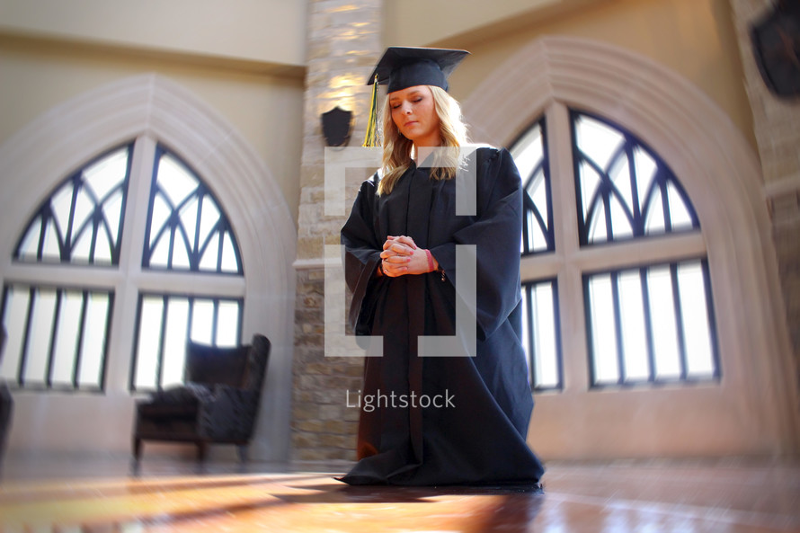 girl in her cap and gown on her knees in prayer