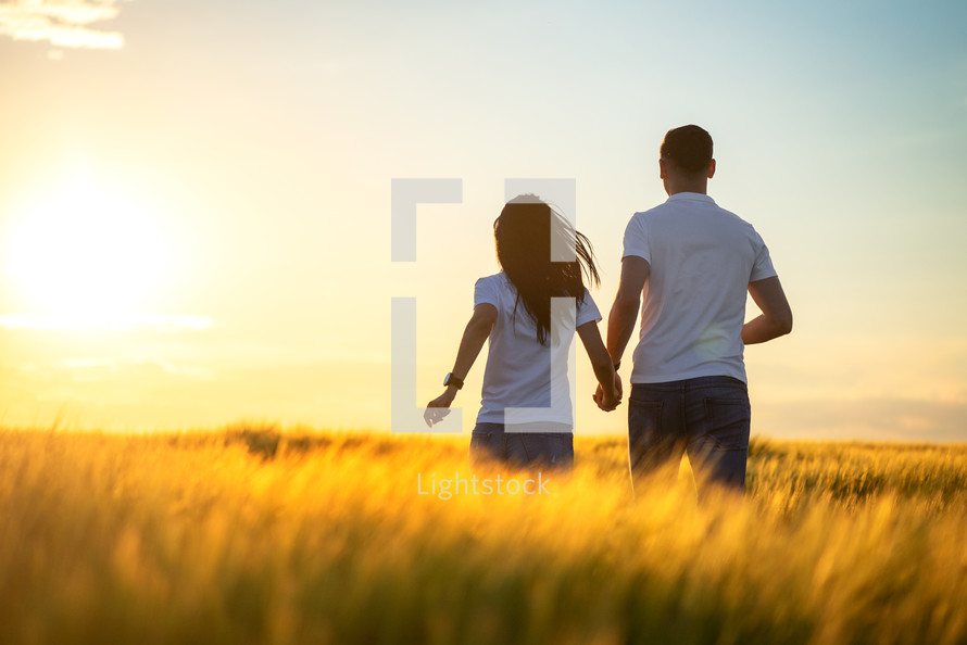 couple standing in a golden field holding hands 