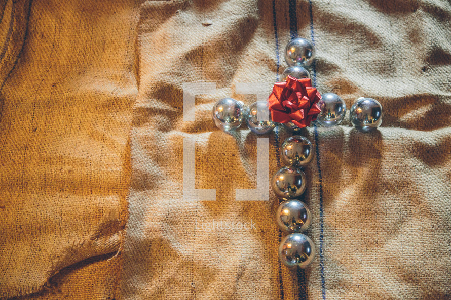 cross of silver Christmas ornaments on burlap 