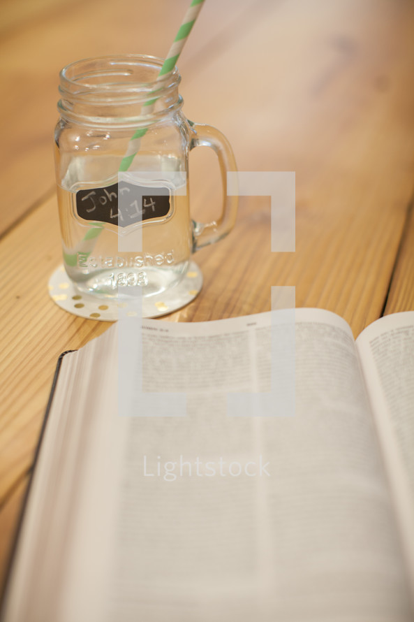 A cup of water with John 4:14 written on it and an open Bible