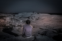 a boy sitting on a rocky shore 