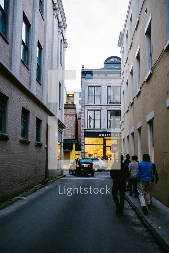 Young men walking down an alley toward retail shops.