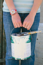woman holding a paint can and brushes out in front of her