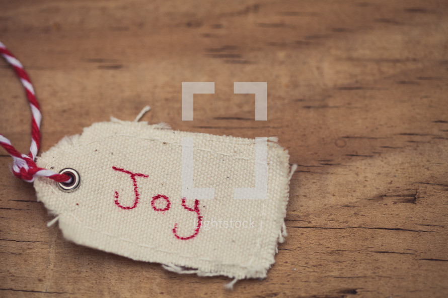 A Christmas gift tags, reading "Joy", on a wood grain background.