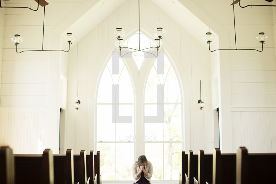 Woman praying in front of a window in a church.