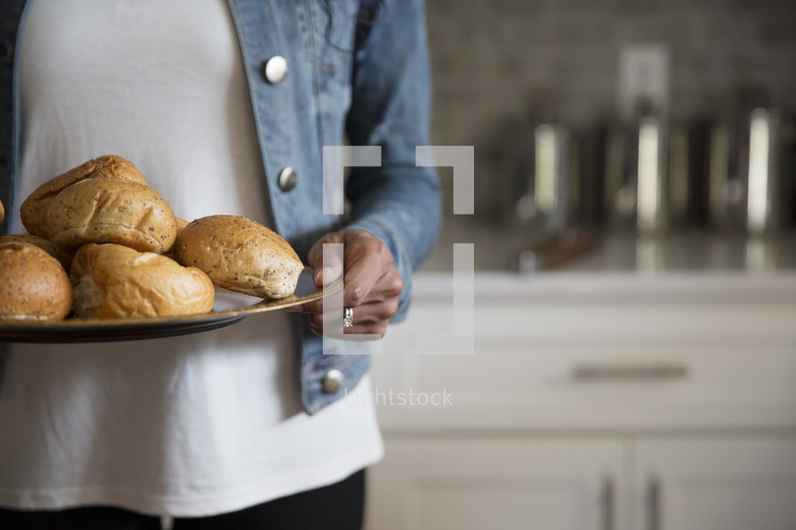 a woman holding a tray of bread buns 
