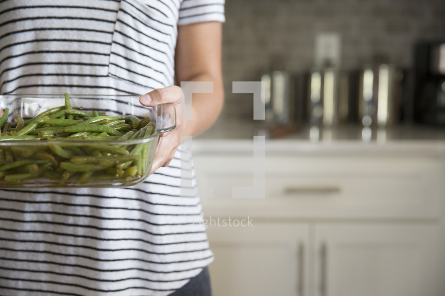 a woman holding green beans in a casserole dish 